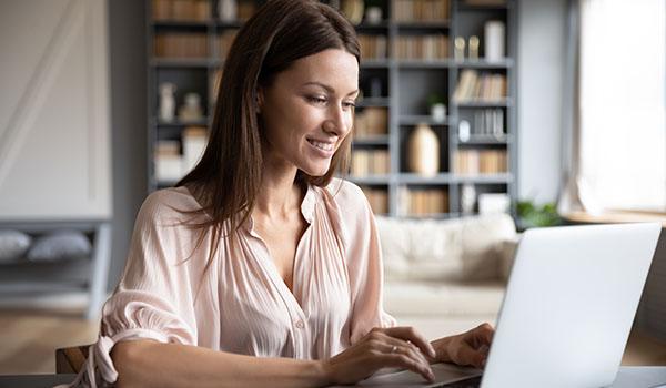 Kvinde der sidder med laptop ved sit spisebord